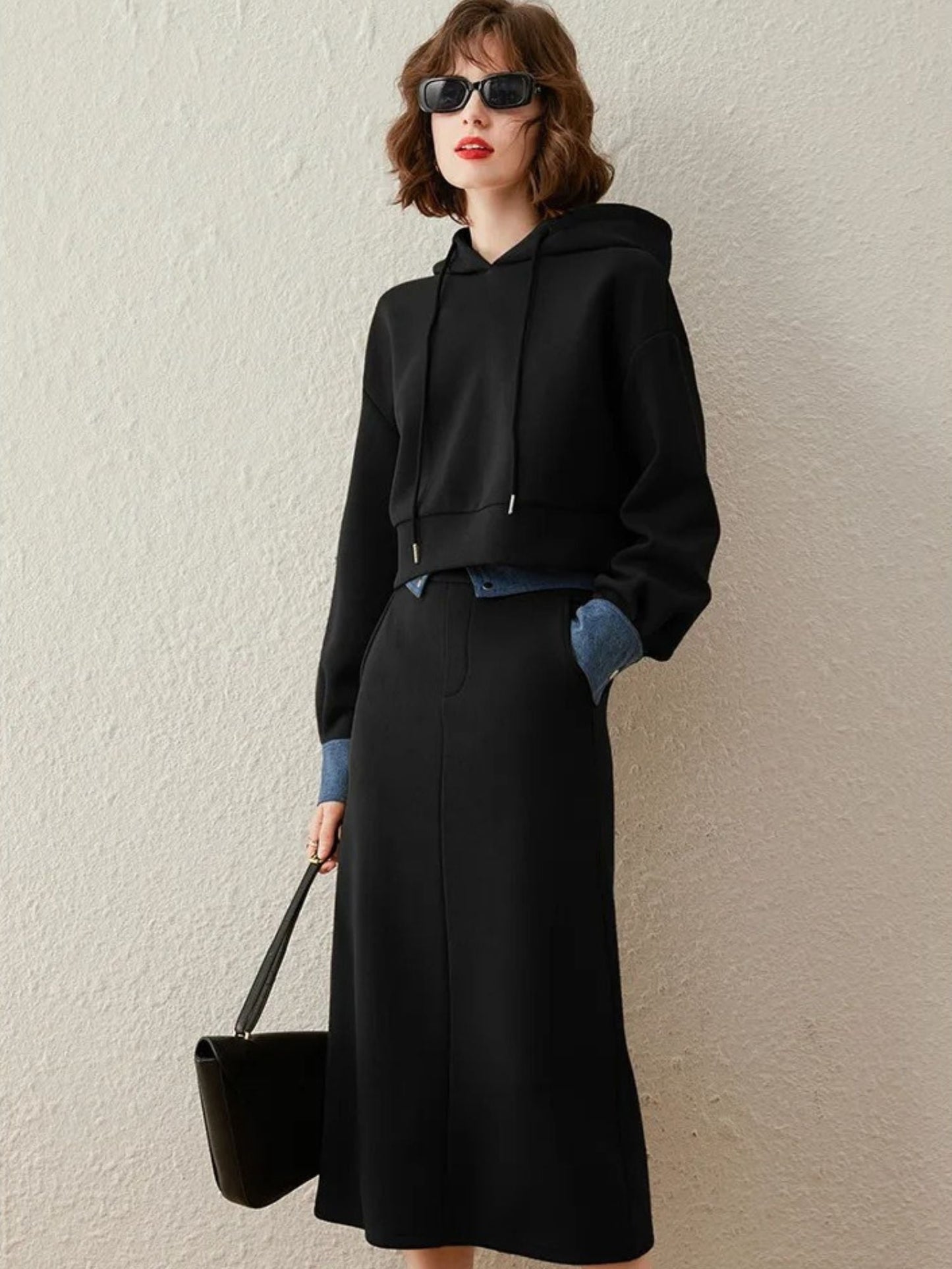 Frau trägt schwarzes Set mit Kapuze, Rock und Sonnenbrille.