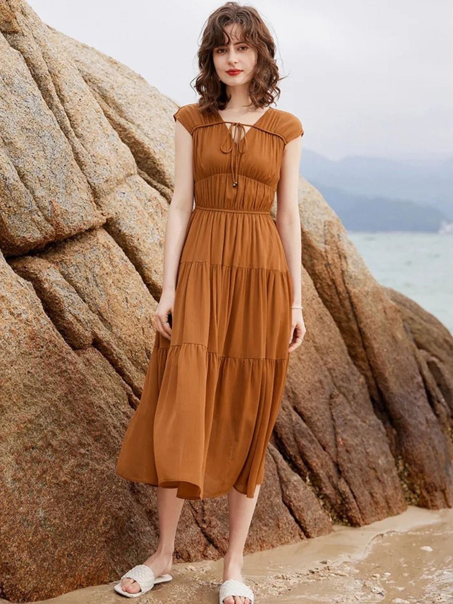 Frau steht vor Felsen im braunen ärmellosen, fließenden Maxikleid.
