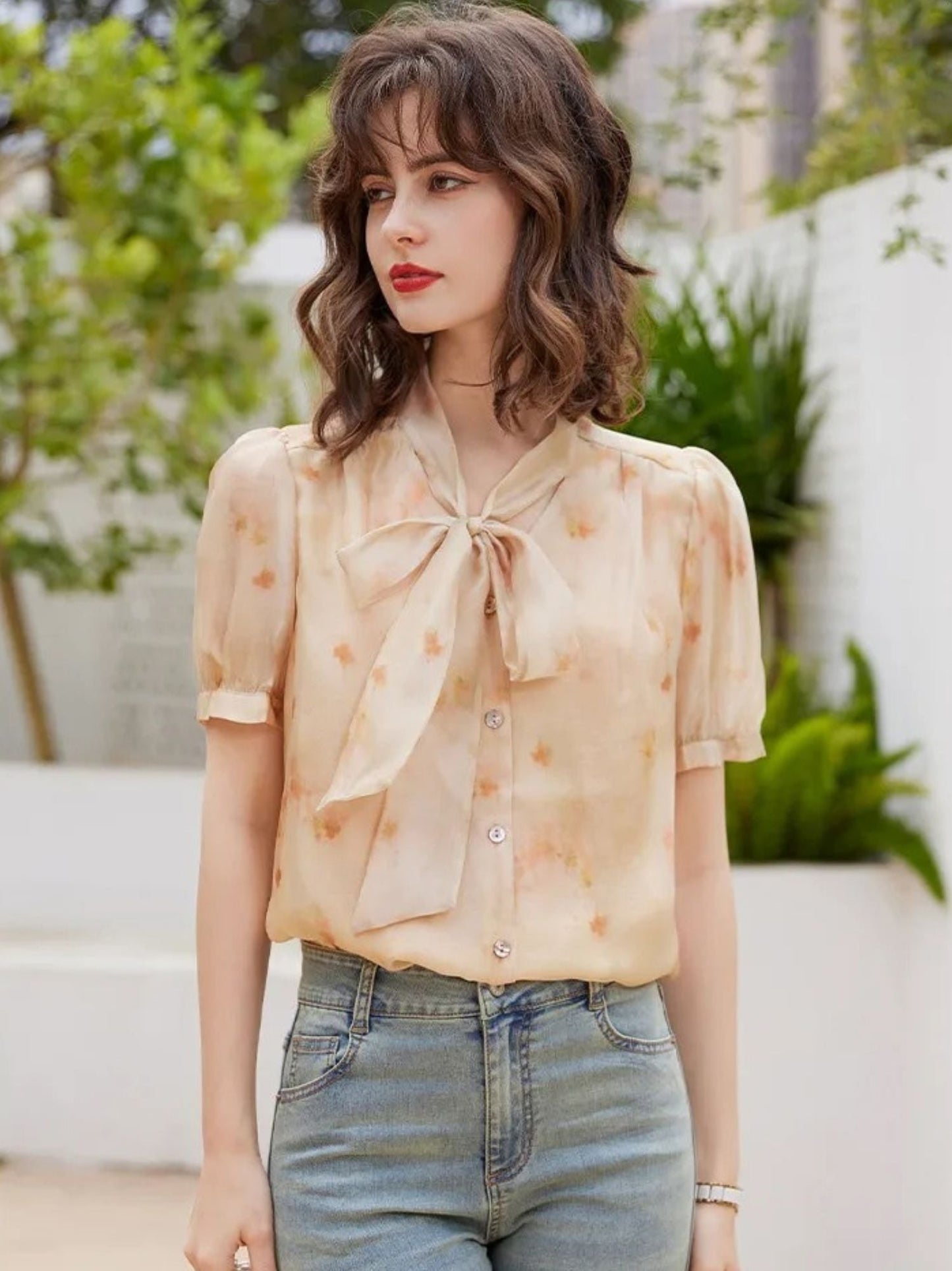 Frontalansicht in pfirsichfarbener Bluse mit Blumenmuster und Jeans.