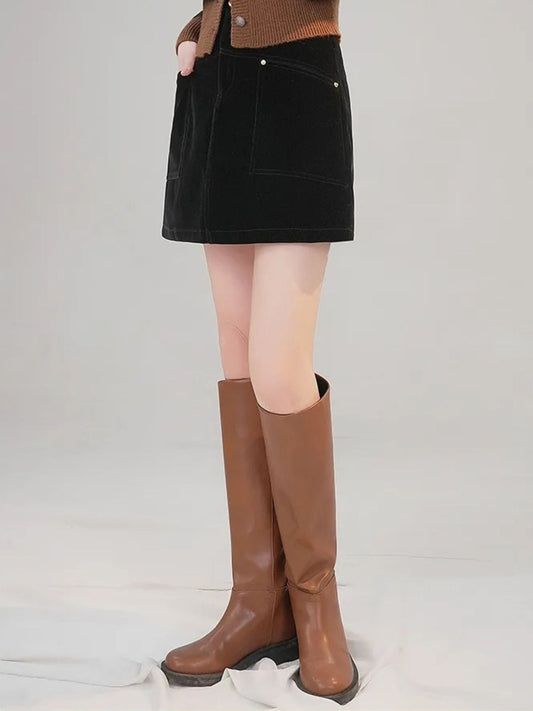 Frau steht im schwarzen Minirock mit braunen Stiefeln.